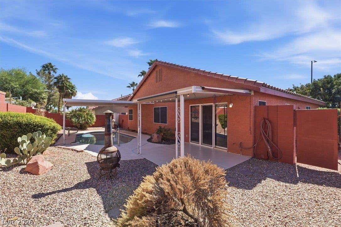 A spacious concrete patio overlooks the private backyard swimming pool under clear blue skies.
