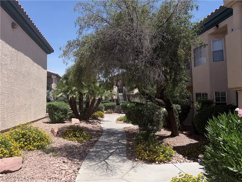 Concrete walkways wind through professionally landscaped grounds featuring mature trees and desert flora.