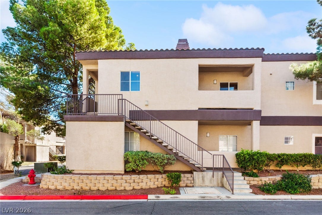 5250 S Rainbow Boulevard, #2033, Las Vegas, NV 89118 Multi-level residential exterior with stucco siding, concrete stairs, and private balconies under a blue sky.