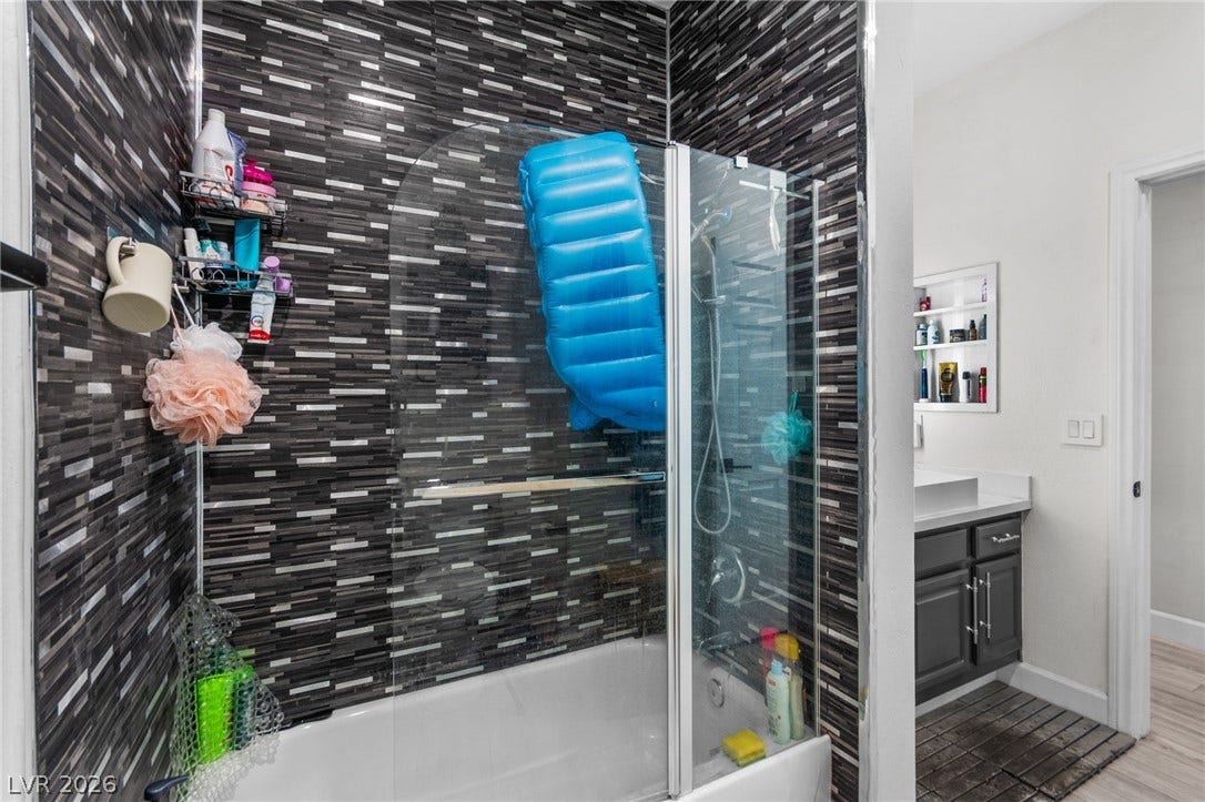 5250 S Rainbow Boulevard, #2033, Las Vegas, NV 89118 Bold mosaic wall tile surrounds a tub and shower enclosure with a glass door.