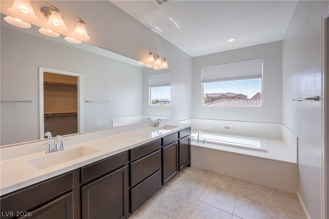 413 Via Gigante, Henderson, NV 89011 A spacious primary bathroom boasts a double vanity, large soaking tub, and tile flooring, offering a serene retreat.