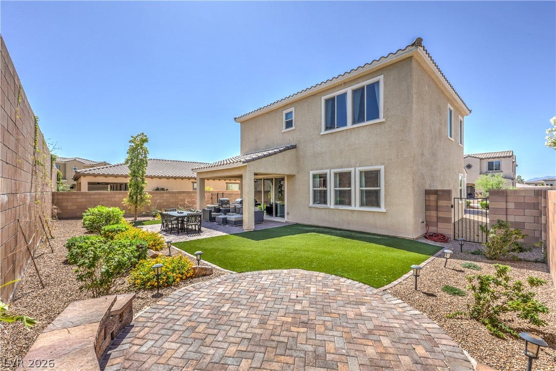 413 Via Gigante, Henderson, NV 89011 A private backyard oasis features a paved patio, covered seating, and artificial turf, perfect for outdoor living.