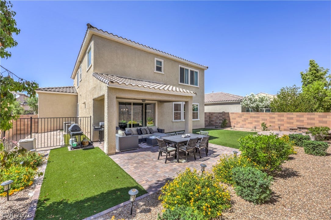 413 Via Gigante, Henderson, NV 89011 A spacious backyard retreat features a covered patio, brick pavers, and vibrant landscaping, perfect for outdoor living.