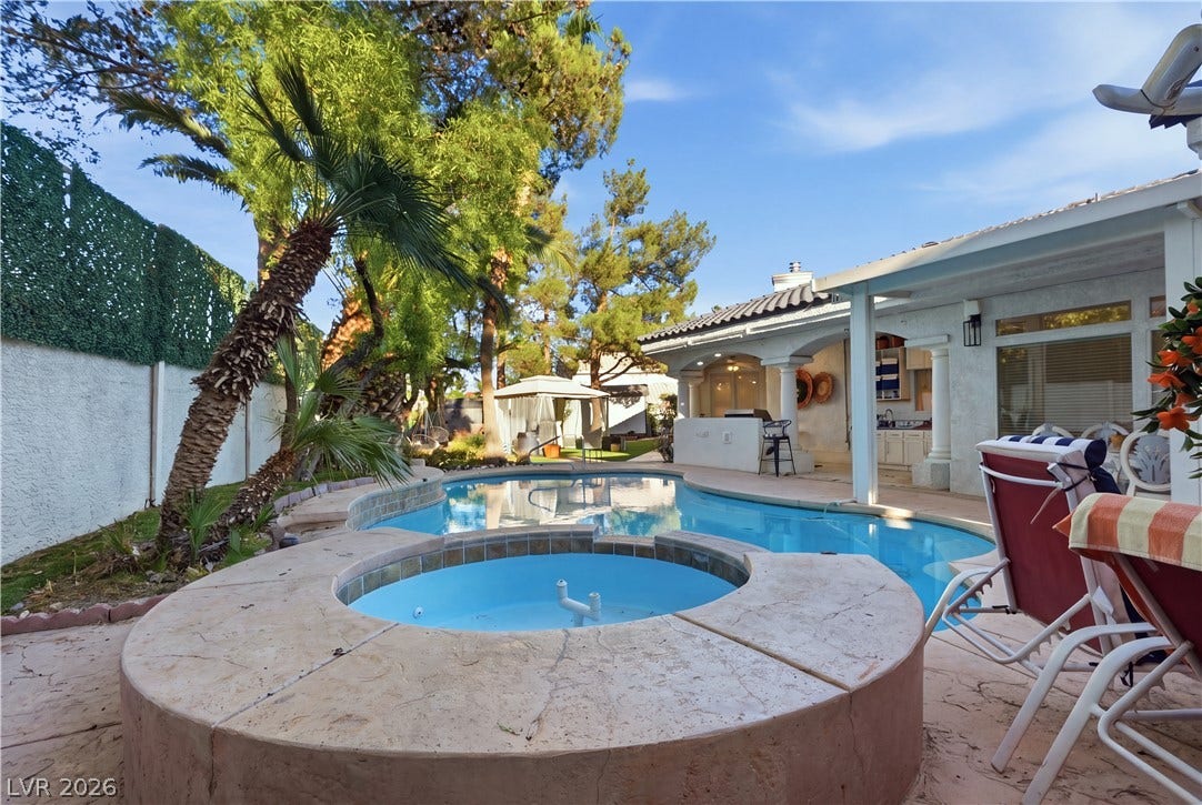 Mature palms frame a sparkling backyard swimming pool and integrated spa under clear skies.