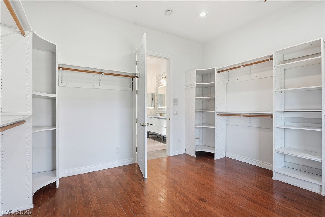 A spacious custom walk-in closet boasts generous built-in shelving and rich hardwood flooring.