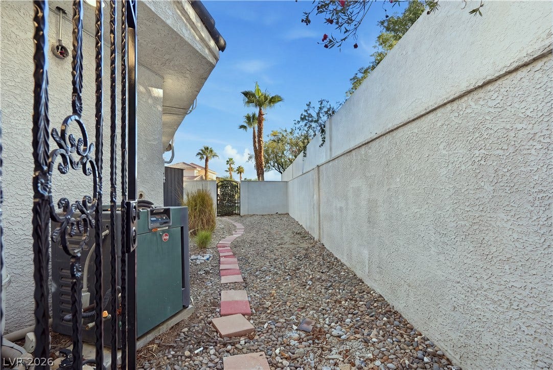 A gravel-lined side yard is bordered by high stucco walls and a decorative gate.