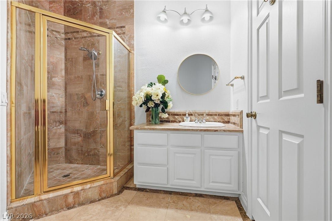 Rich stone tile highlights a glass-enclosed shower and adjacent single vanity.