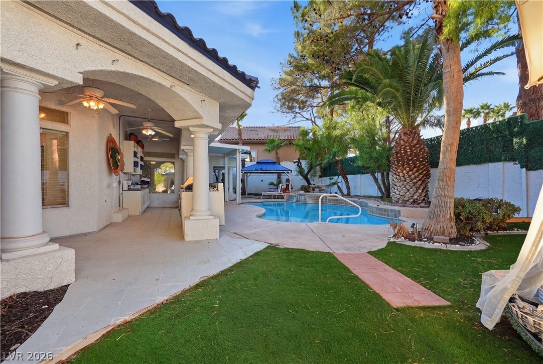 An inviting covered patio steps down to a private swimming pool framed by mature palms.
