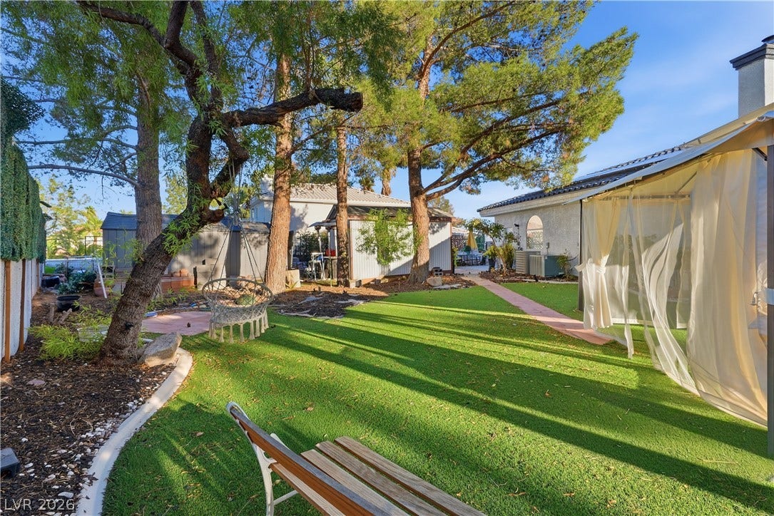 Mature trees shade a landscaped lawn bordered by garden structures and paved walkways.