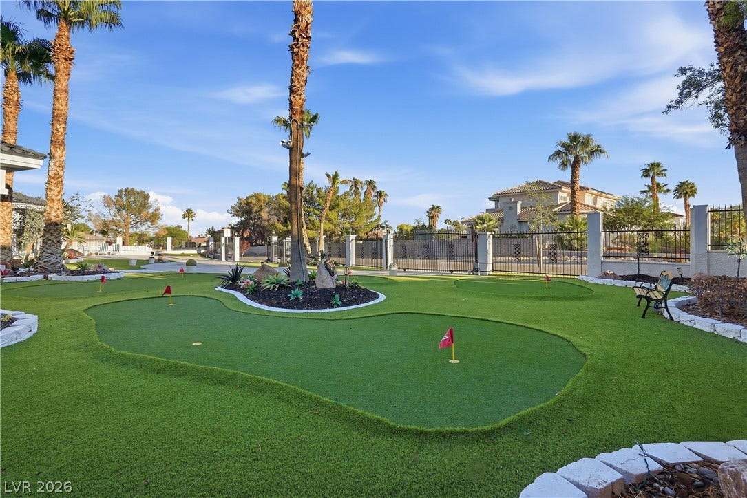 A private backyard putting green offers outdoor recreation under towering palm trees.