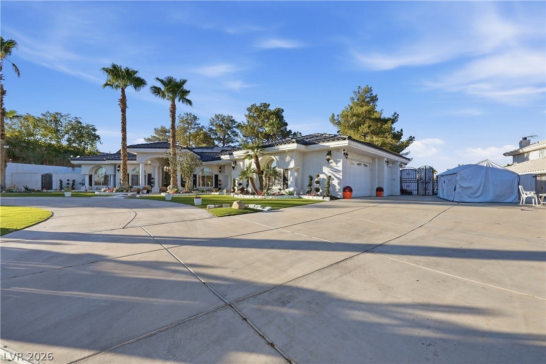 A spacious concrete driveway leads toward the grand stucco exterior of this luxury single-level estate.