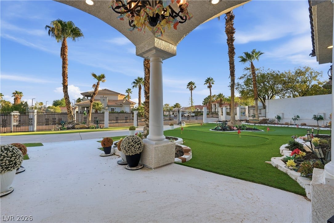 A spacious covered patio overlooks a manicured putting green framed by towering palm trees.