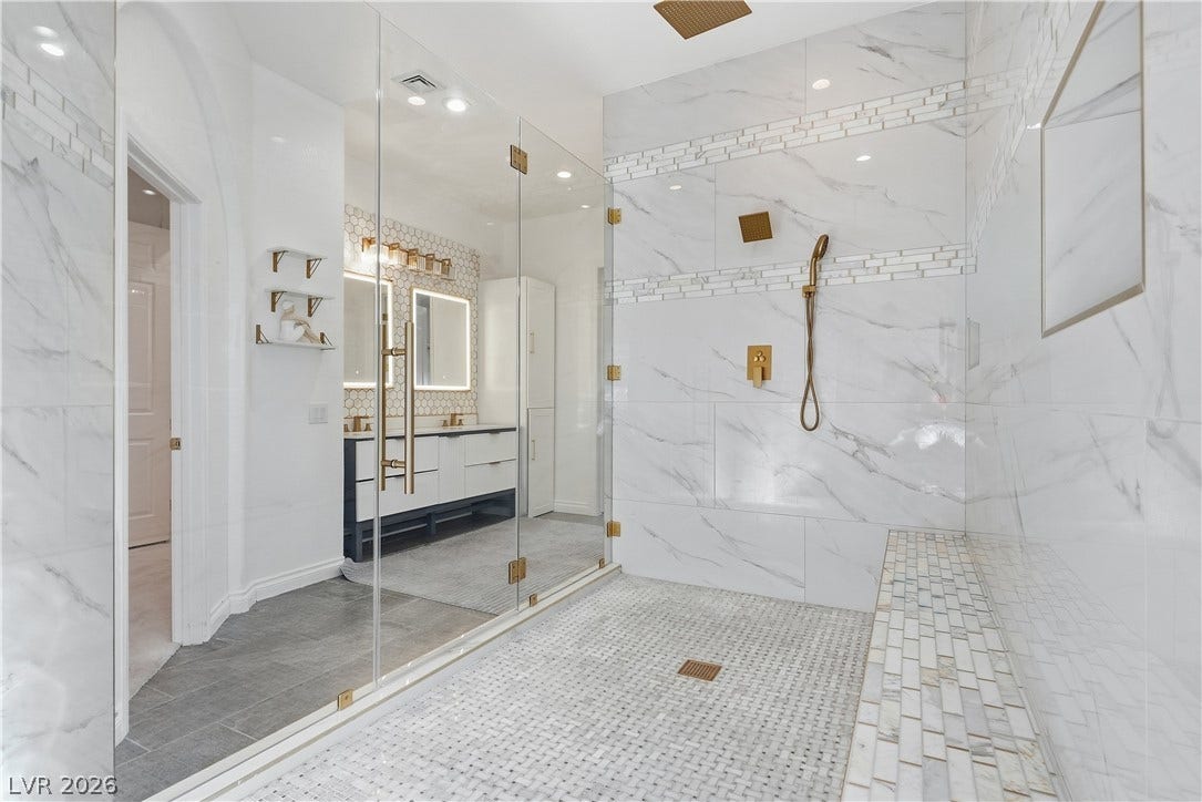 Floor-to-ceiling marble tile and gold fixtures elevate this massive walk-in shower.