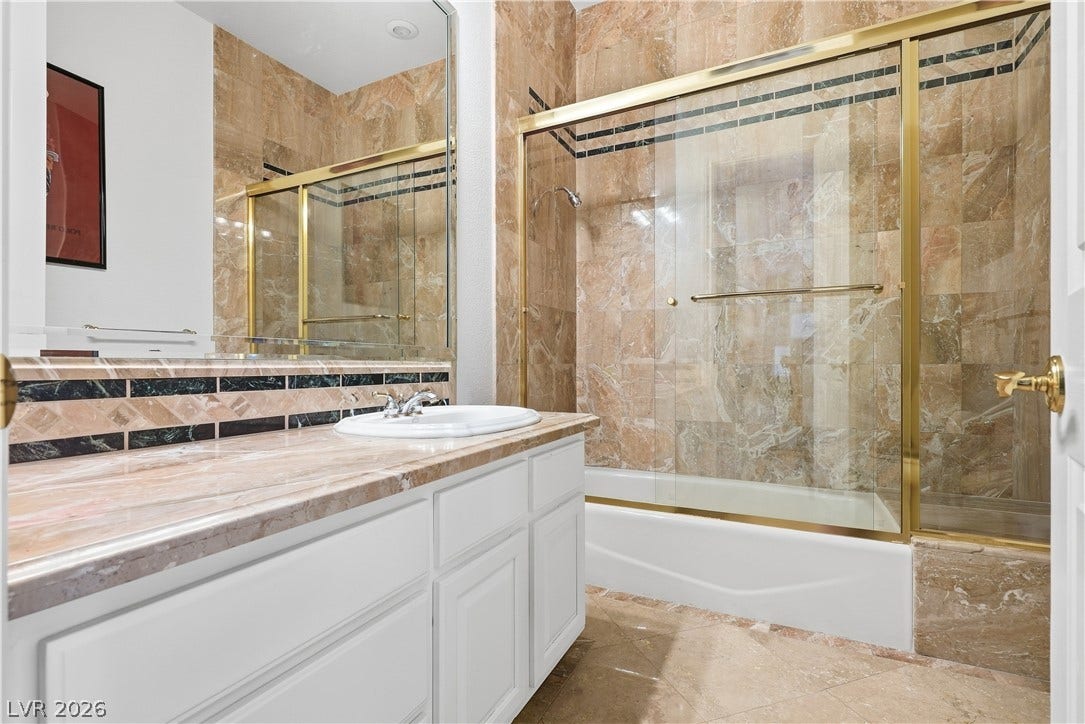 Polished stone counters and matching wall tile elevate this bathroom featuring a glass shower enclosure.