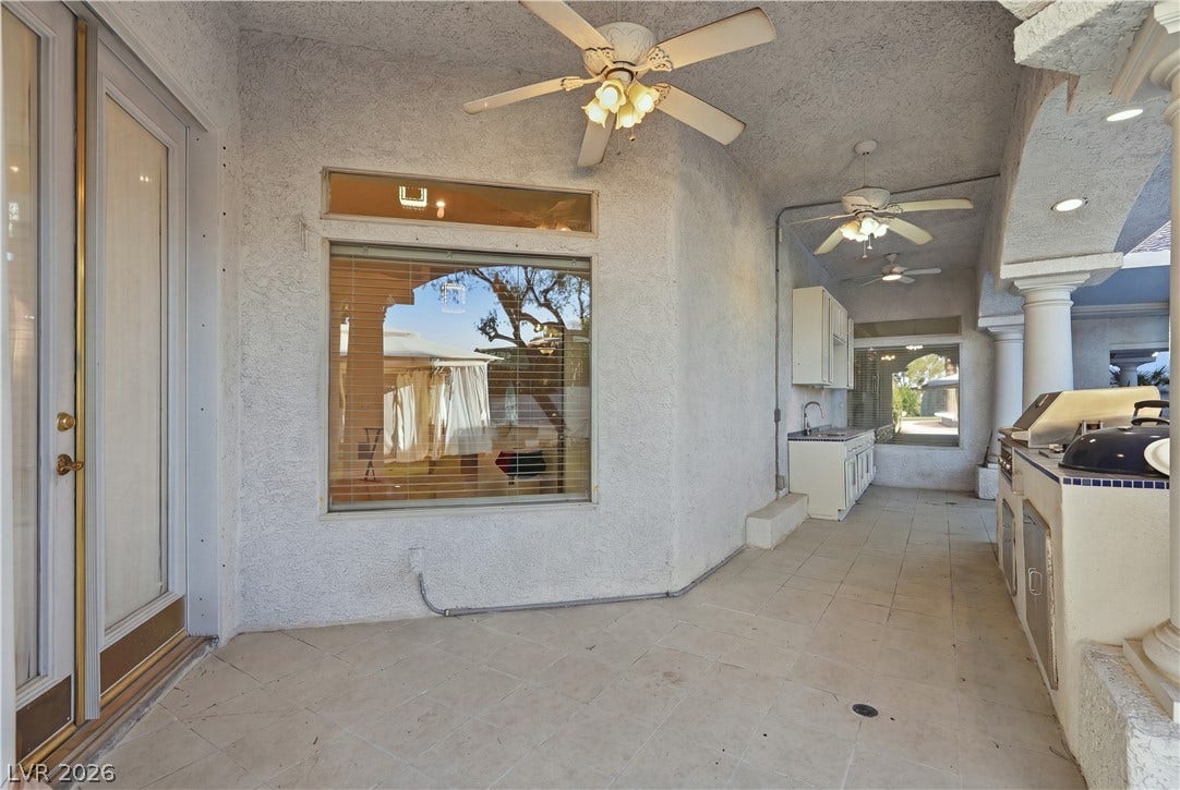 A spacious covered patio features an outdoor kitchen setup alongside durable tiled flooring.