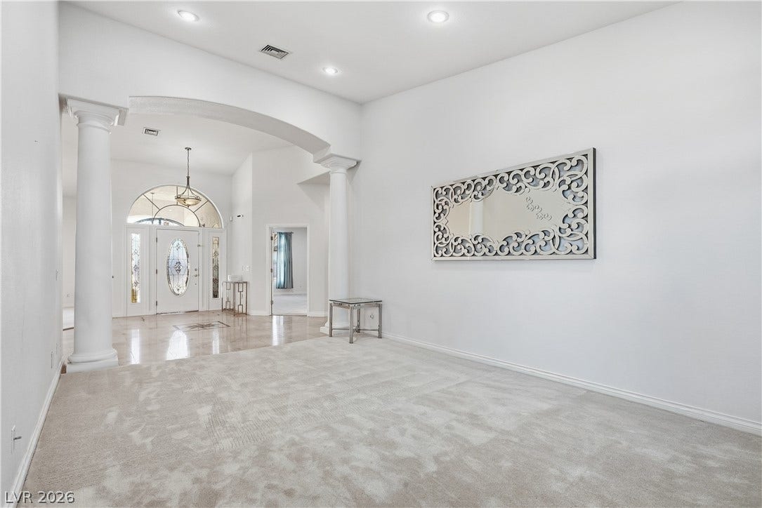 An arched transition with classic columns links this carpeted space to a tiled foyer.