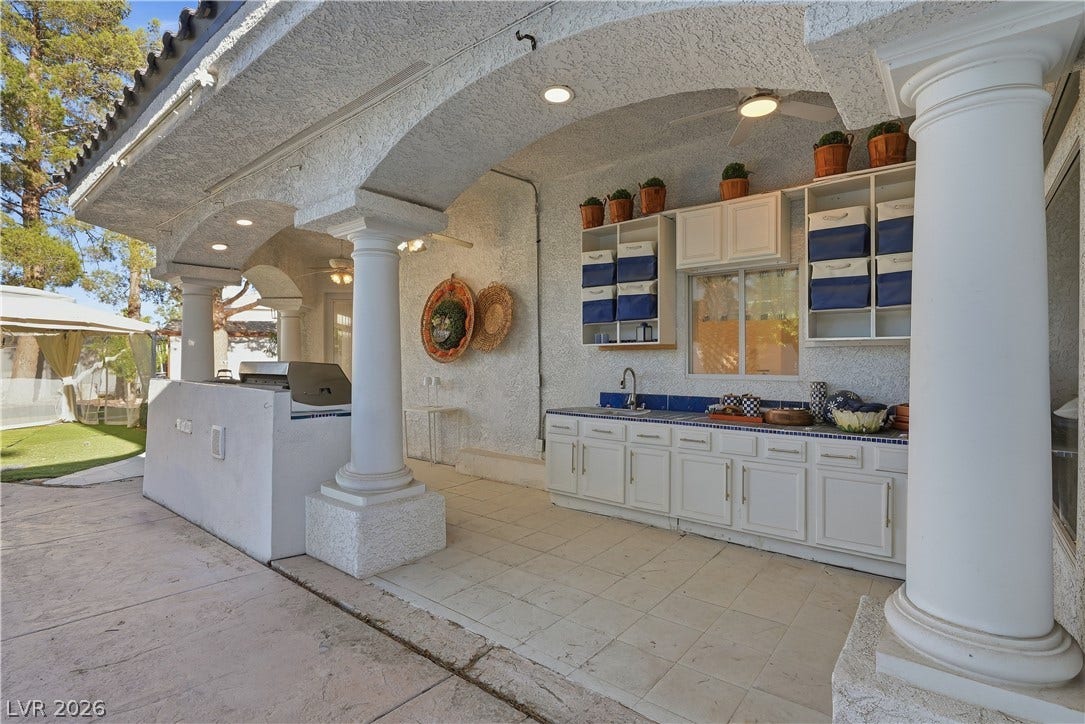 Arched stucco pillars frame a spacious covered outdoor kitchen and prep area.