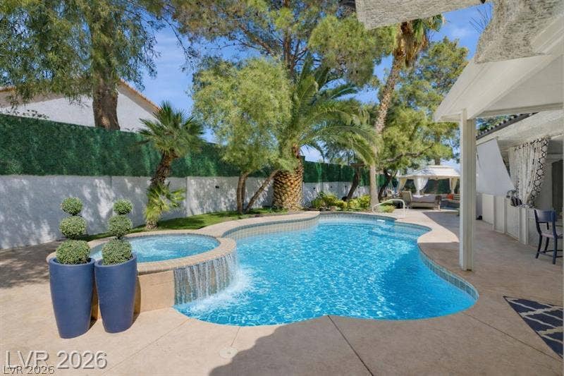 A sparkling swimming pool and integrated spa sit surrounded by a spacious concrete patio.