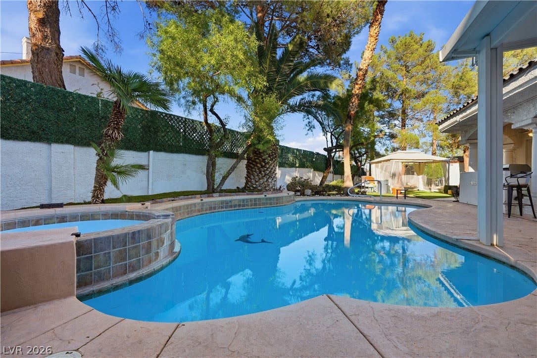 Lush tropical palm trees frame a shimmering swimming pool alongside a raised tile spa.
