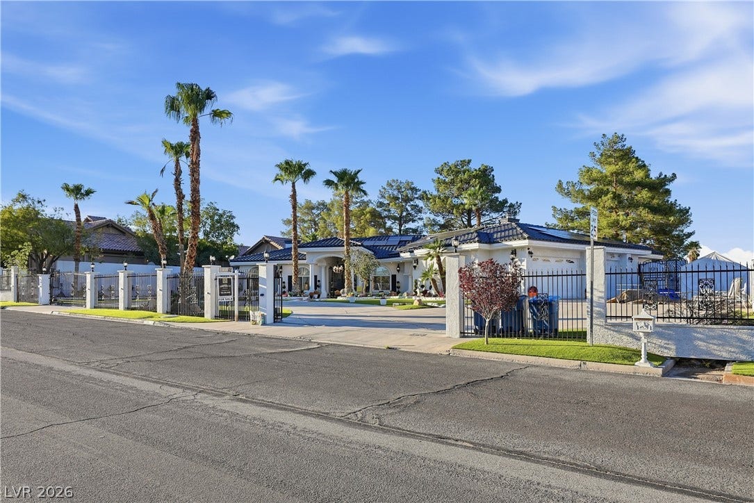 Secure wrought iron fencing surrounds this sprawling single-story estate framed by mature palm trees.