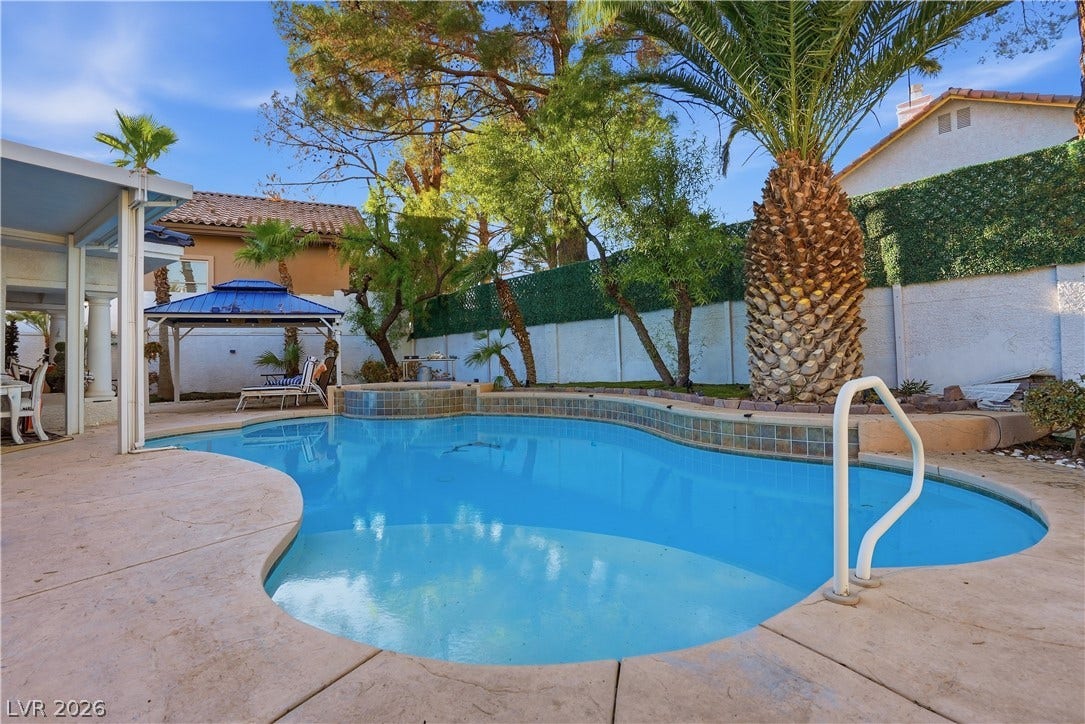 Mature palms and a concrete patio frame this sparkling backyard swimming pool and spa.