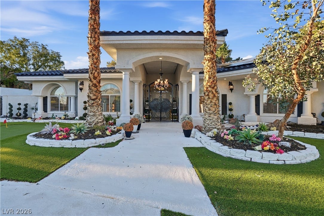 An arched portico with prominent columns and custom wrought-iron gates creates an inviting entrance.