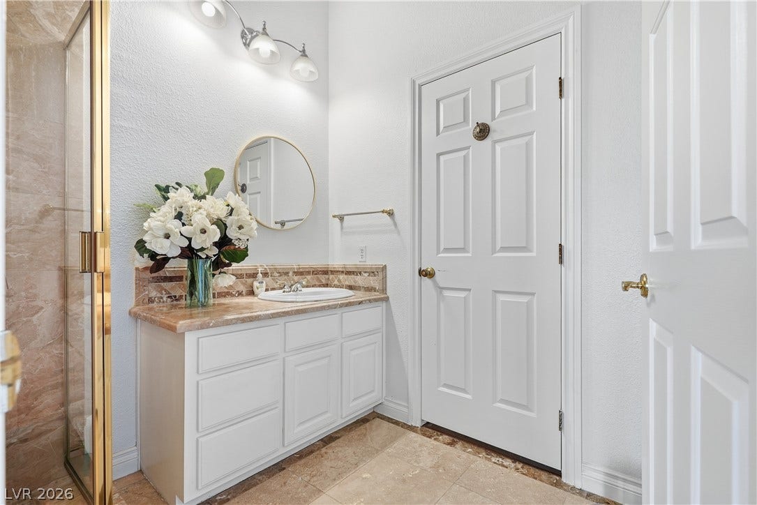 Stone countertops and a glass-enclosed shower highlight this pristine, light-filled bathroom space.