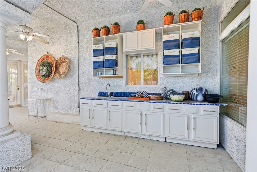 An outdoor kitchen setup on a covered patio features tile flooring and custom white cabinetry.