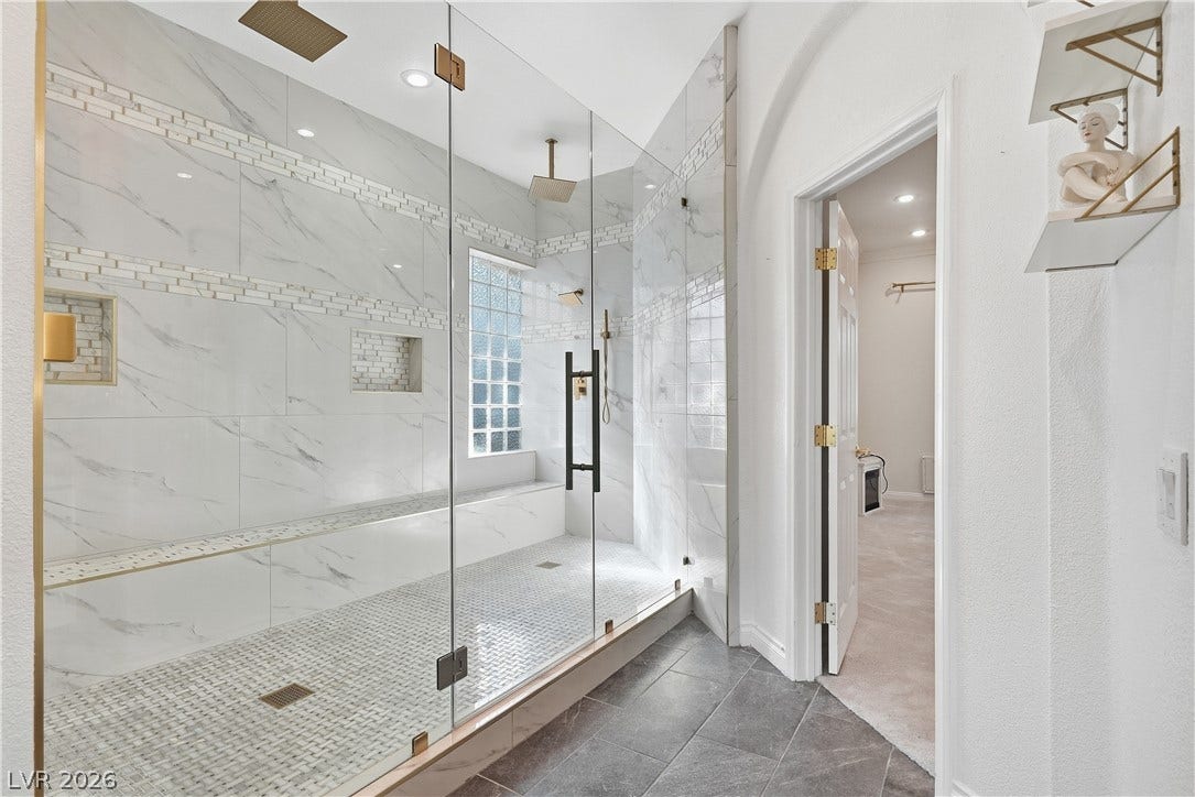 Floor-to-ceiling marble tile surrounds a massive walk-in shower with dual brass rain showerheads.