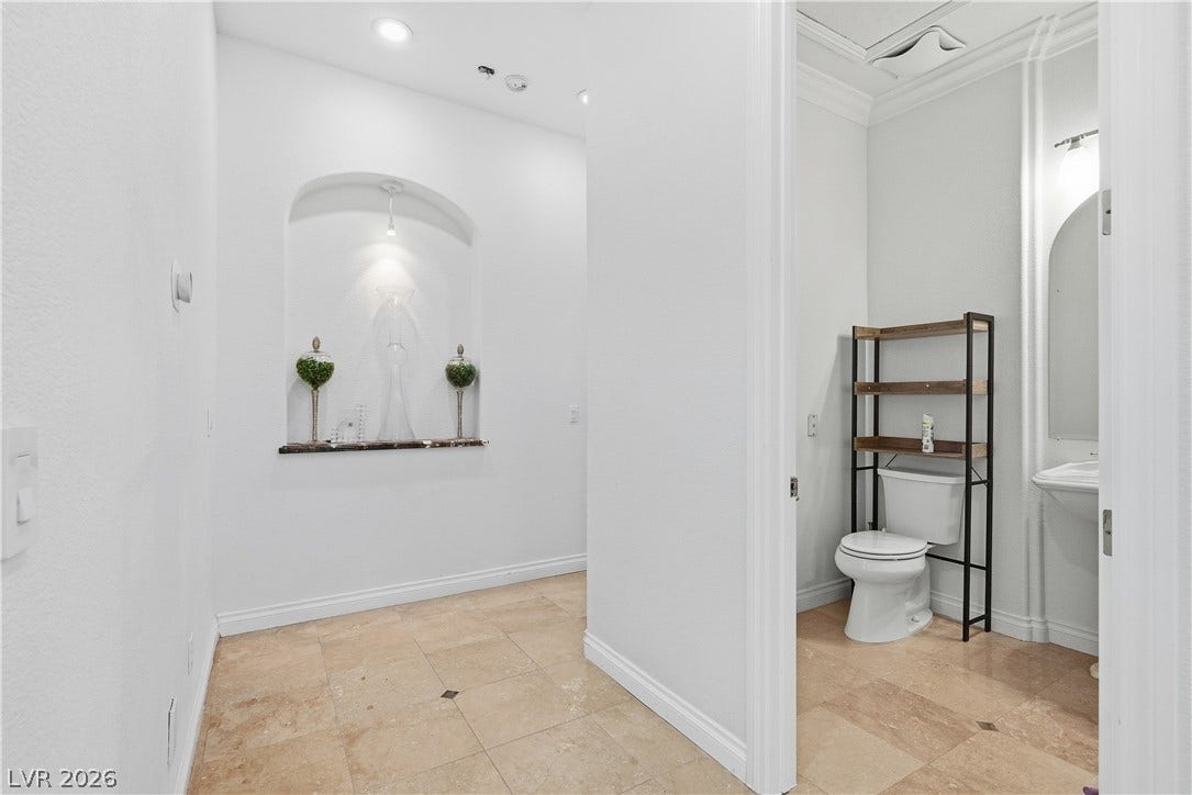 Gleaming tile floors and an arched wall niche elevate this hallway leading to a powder room.