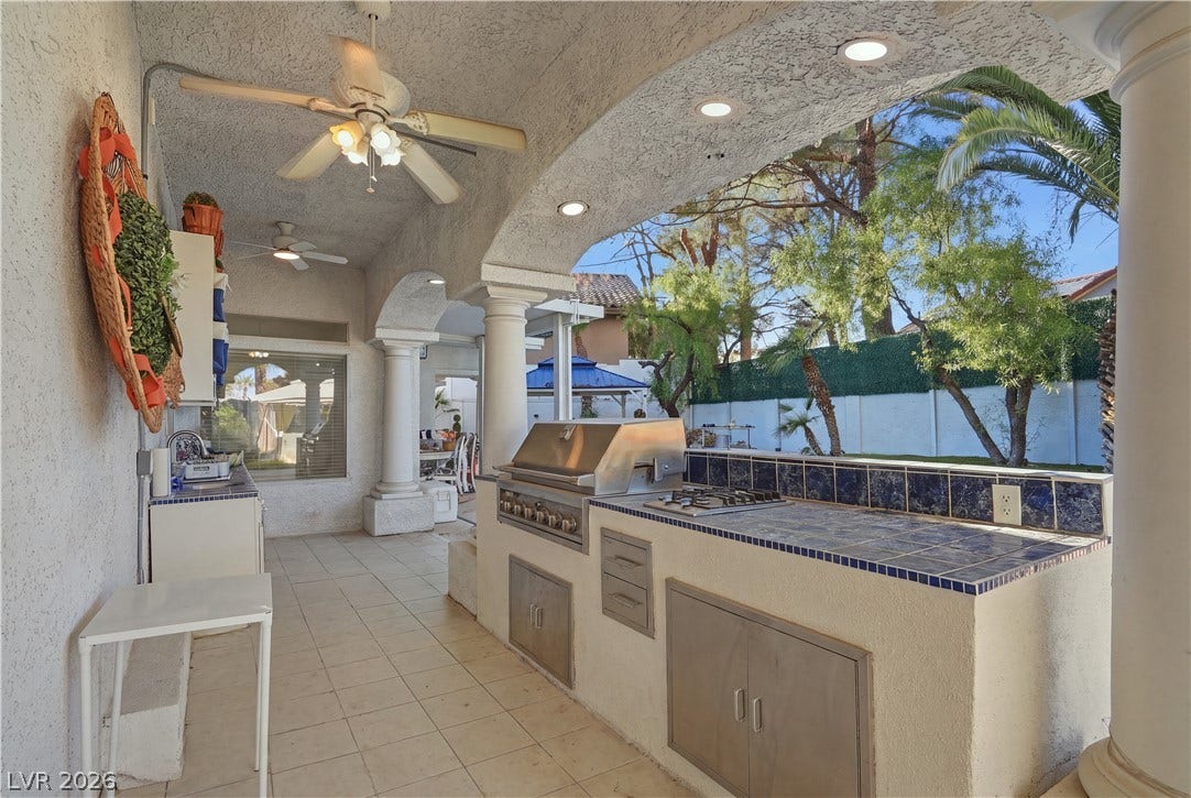 An arched patio cover shelters a tiled outdoor kitchen complete with built-in appliances.