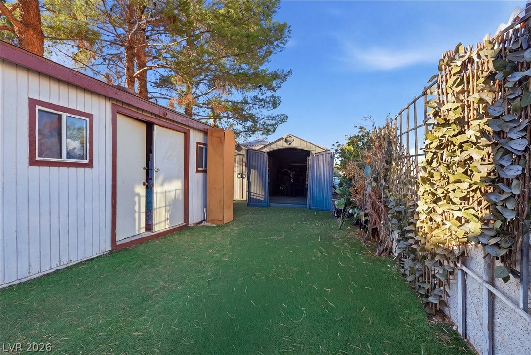 Functional outdoor storage buildings flank a grassy side yard lined by a leafy privacy fence.