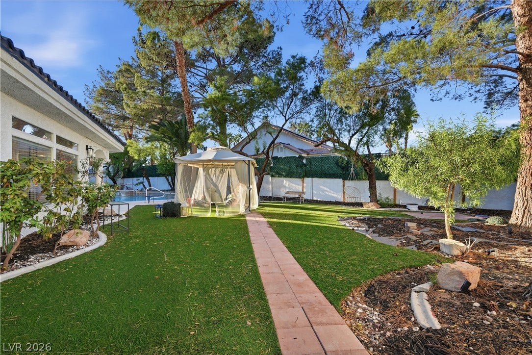 Mature trees frame a manicured green lawn featuring a paved stone walkway and shaded gazebo.