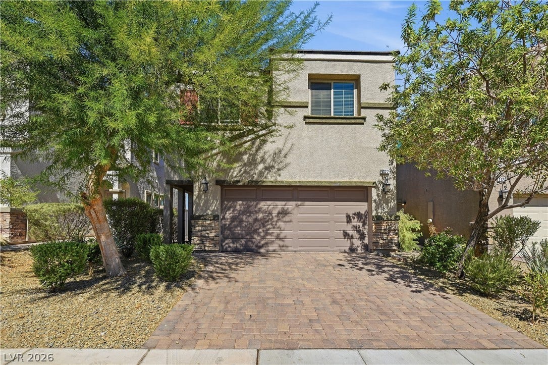 1122 Bradley Bay Avenue, Henderson, NV 89014 Mature trees frame a charming two-story stucco exterior featuring a paved driveway and garage.