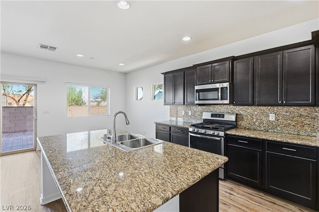1122 Bradley Bay Avenue, Henderson, NV 89014 Granite countertops and dark cabinetry anchor a kitchen illuminated by recessed lighting.