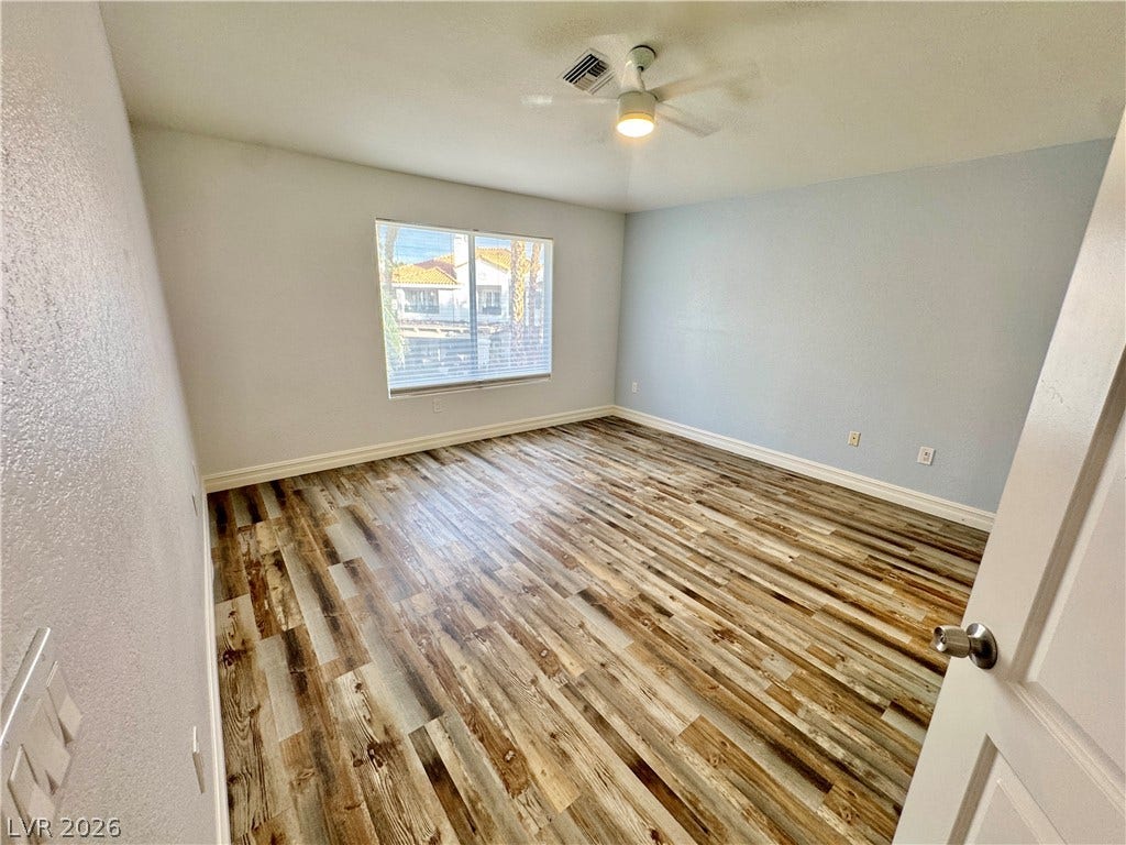Richly textured wood-look flooring anchors this airy bedroom space lit by a wide front-facing window.