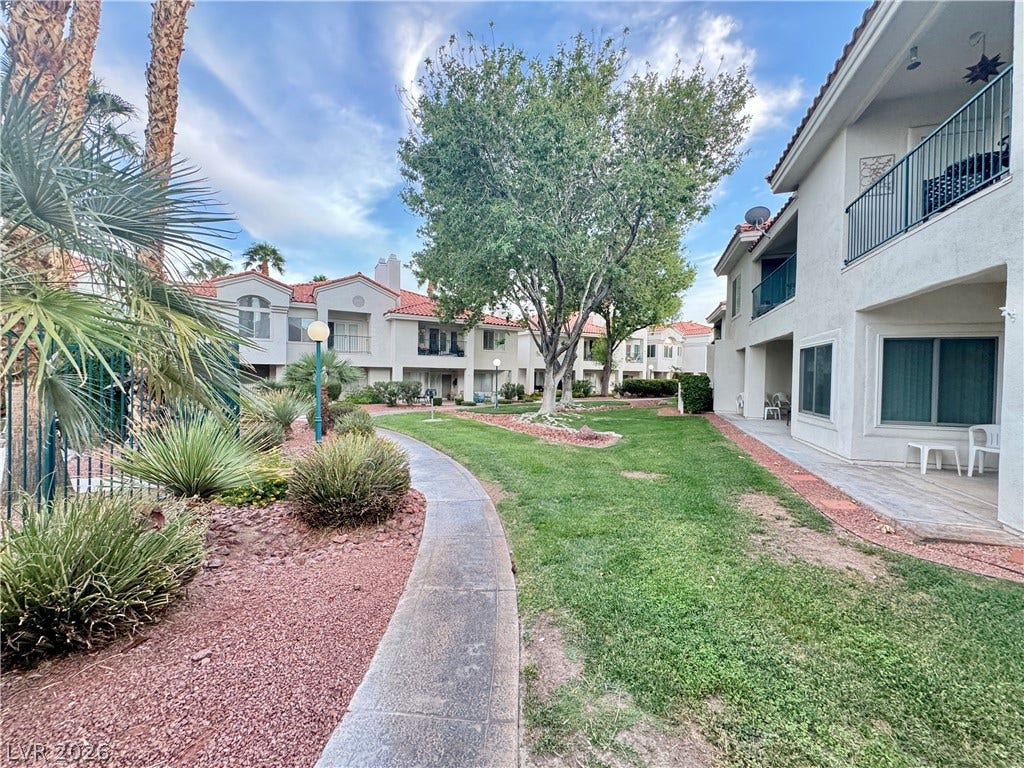 Manicured green spaces and winding concrete pathways connect these stucco multi-family residential structures.