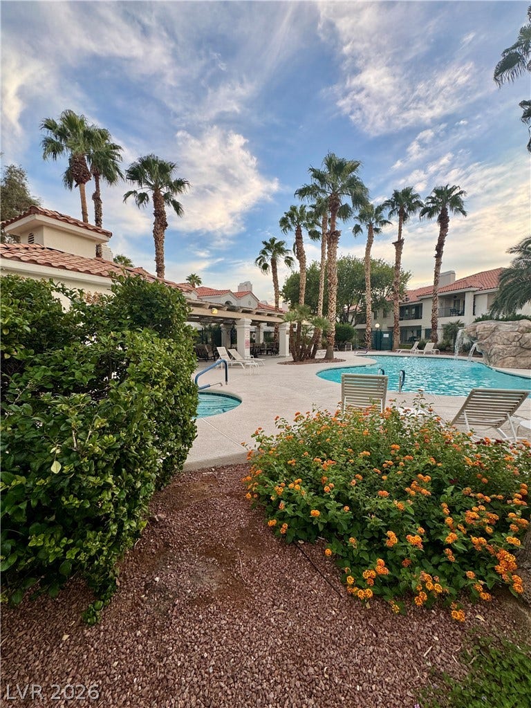 Lush tropical landscaping surrounds a sparkling community swimming pool with integrated spa and rock waterfall.