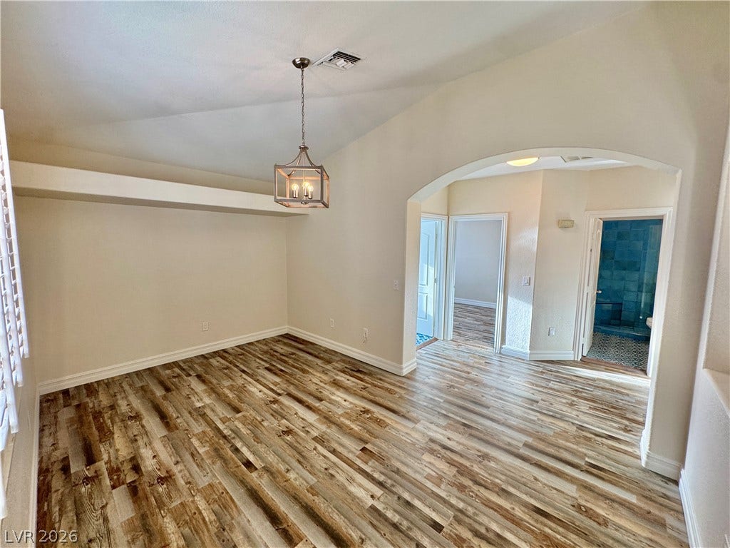 Rich wood-textured flooring flows beneath a vaulted ceiling highlighted by a distinctive arched entryway.