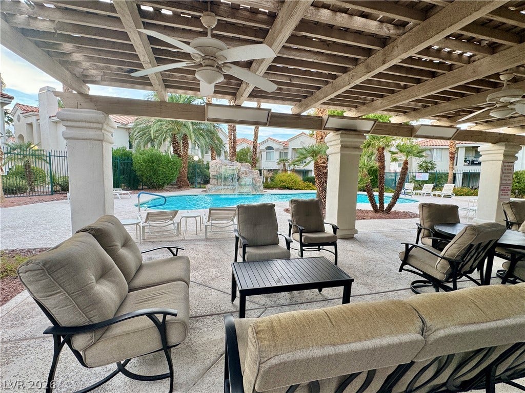 A shaded patio structure overlooks a community pool area with palm trees.