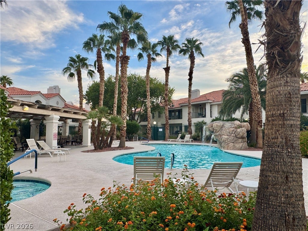 Lush palm trees surround a sparkling blue swimming pool with a rocky waterfall feature.