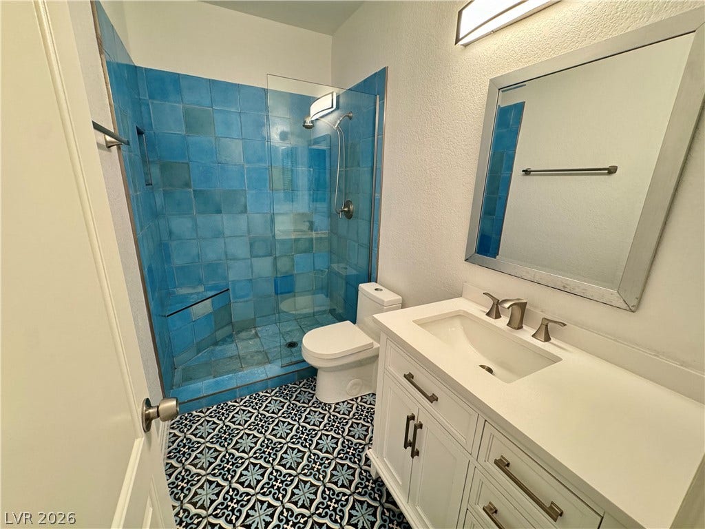 Patterned floor tile and a vibrant tiled shower stall define this modern bathroom space.