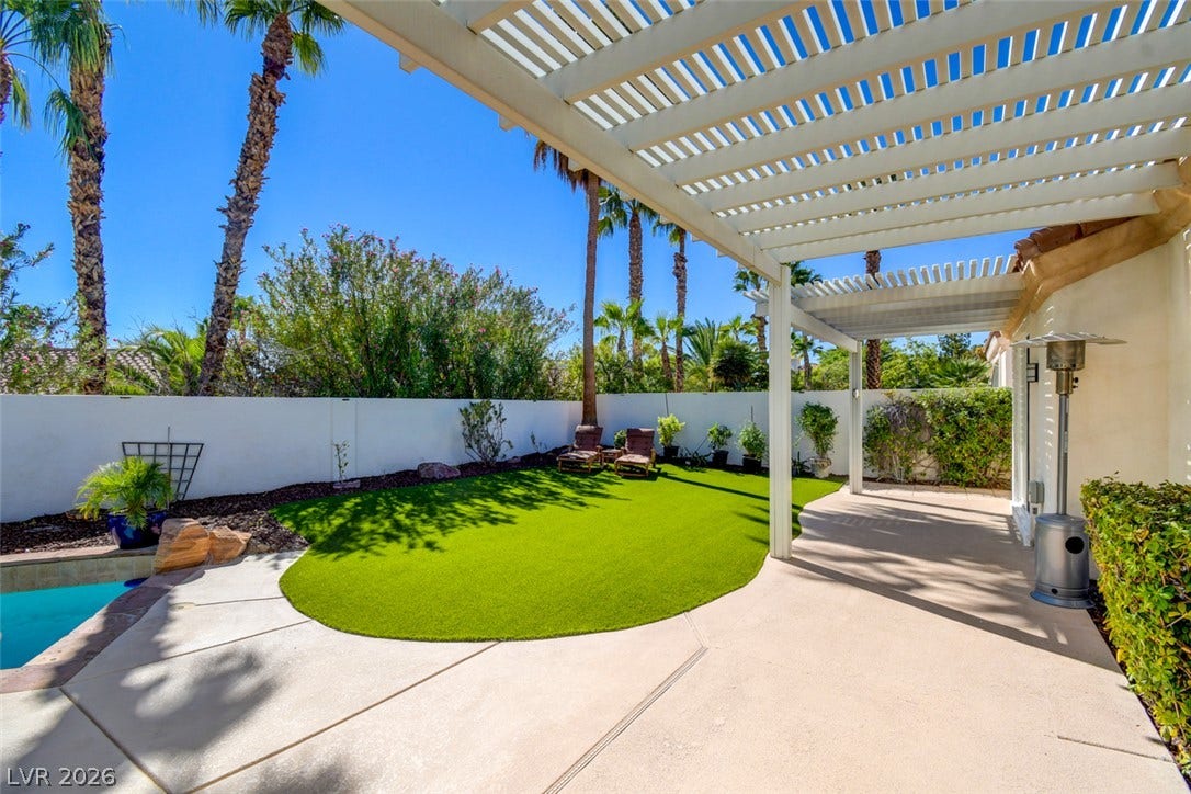 An inviting backyard patio sheltered by a classic pergola overlooks a tidy lawn and pool.