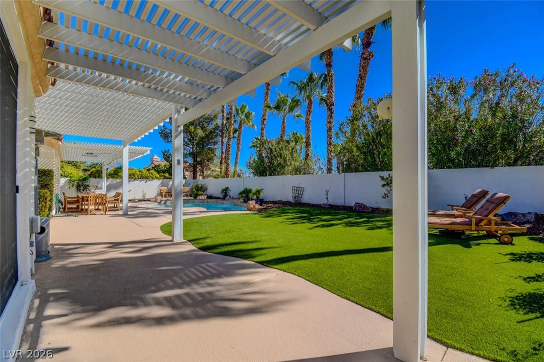 An inviting backyard oasis features a shaded patio structure alongside a sparkling swimming pool.