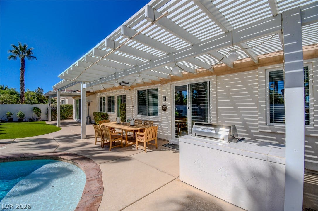 An expansive patio features a white pergola alongside a built-in barbecue and private pool.