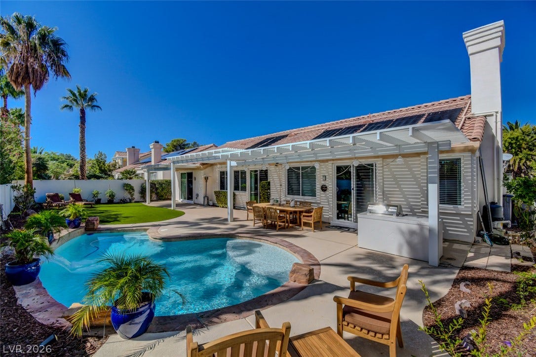 An inviting backyard pool oasis features a spacious concrete patio under a classic white pergola.