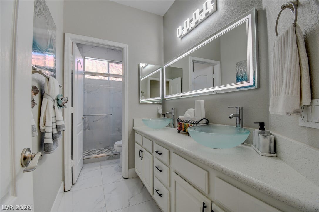 A sleek double vanity with vessel sinks stands adjacent to a tiled walk-in shower.