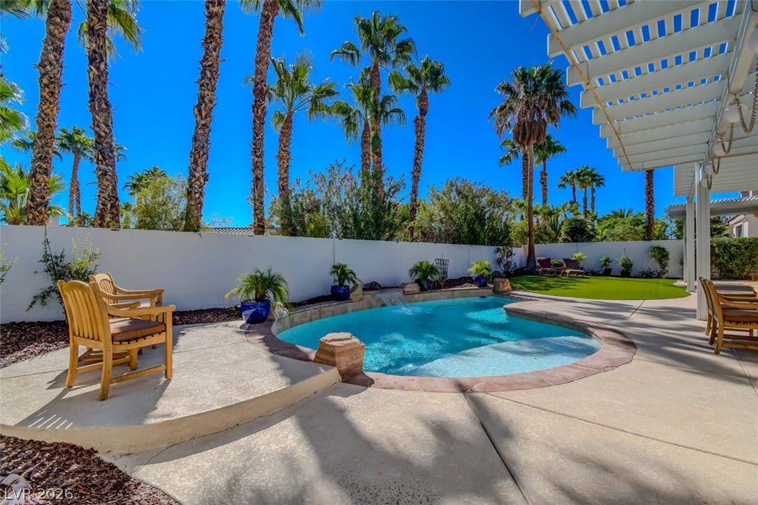 Soaring palm trees frame a sparkling inground pool and spacious concrete patio under clear blue skies.