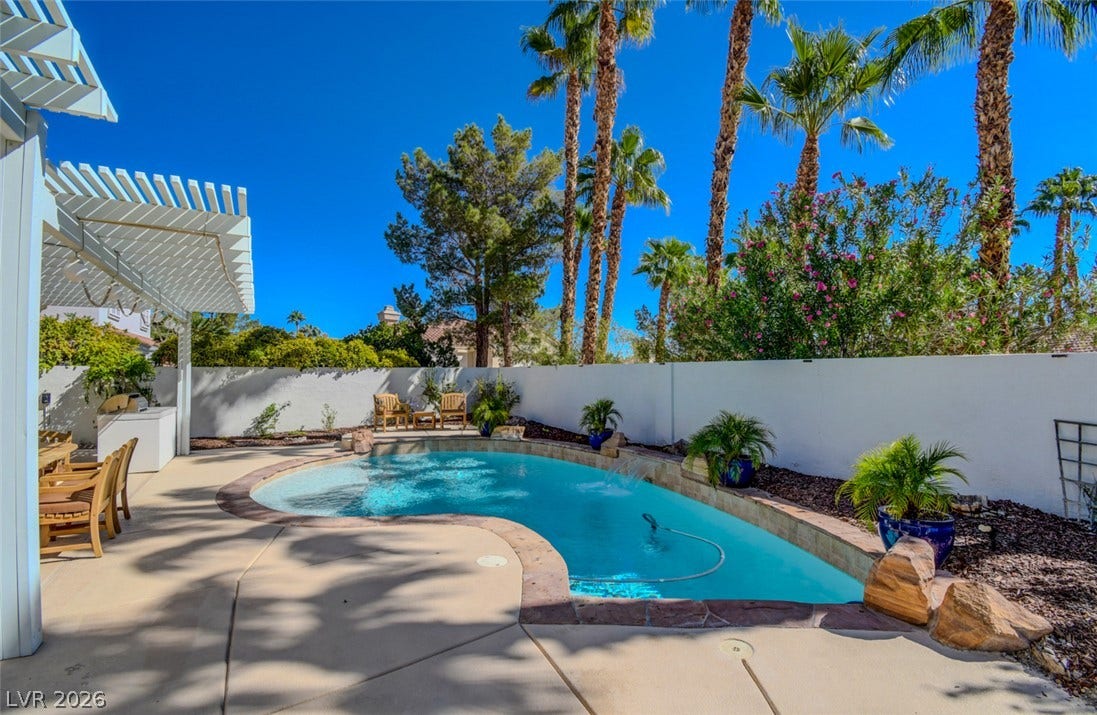 Mature palms frame a sparkling backyard pool surrounded by concrete decking and a trellis.