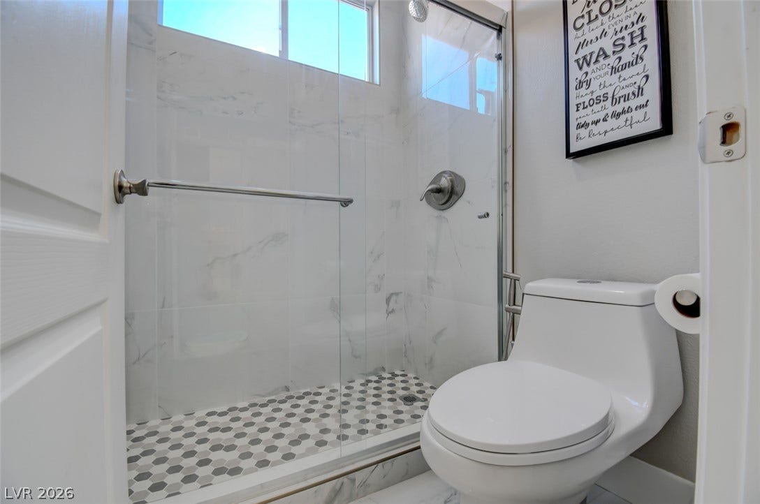A glass-enclosed shower showcases marble-patterned wall tiles and patterned mosaic floor tiling.